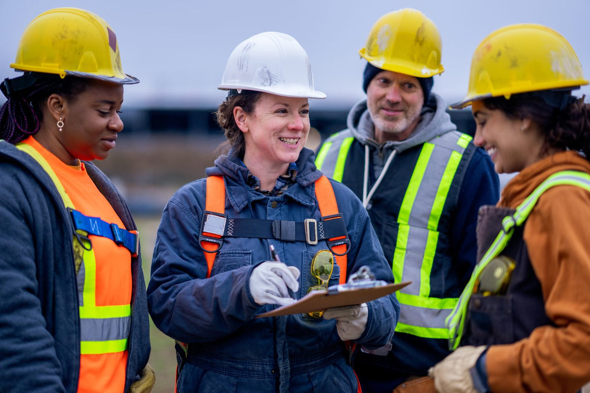 Construction crew in hard hats and safety vests reviewing a clipboard on a job site